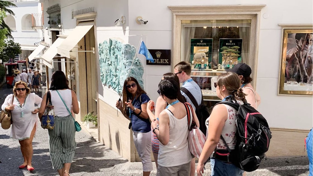 Tour group exploring a street in Capri Island with a guide holding a flag.