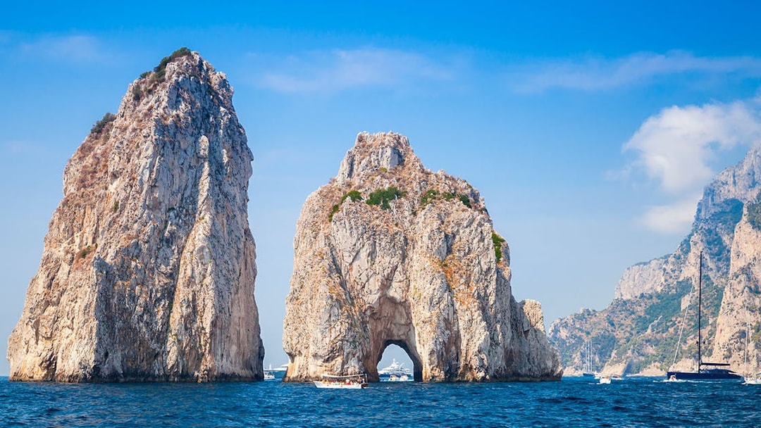 Faraglioni rock formations in Capri with boats in the surrounding blue sea.