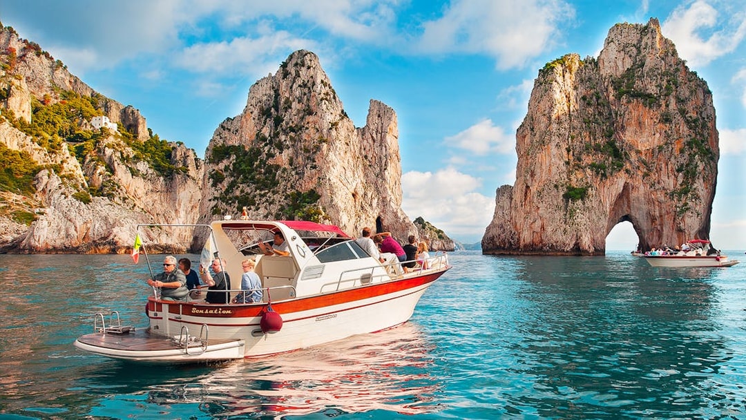 Boat tour near Faraglioni rock formations, Capri, Italy.