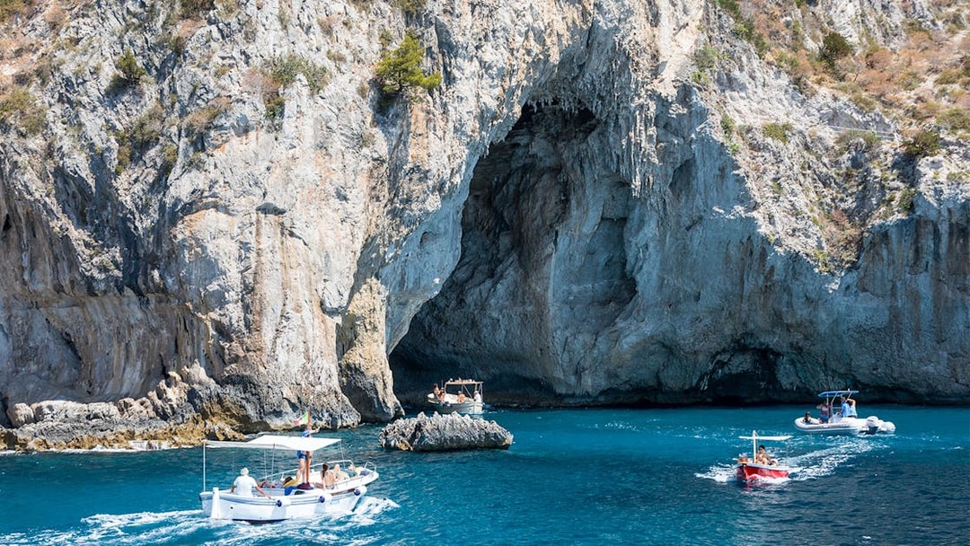 Boats navigating near a rocky cave on the coast of Capri, Italy.