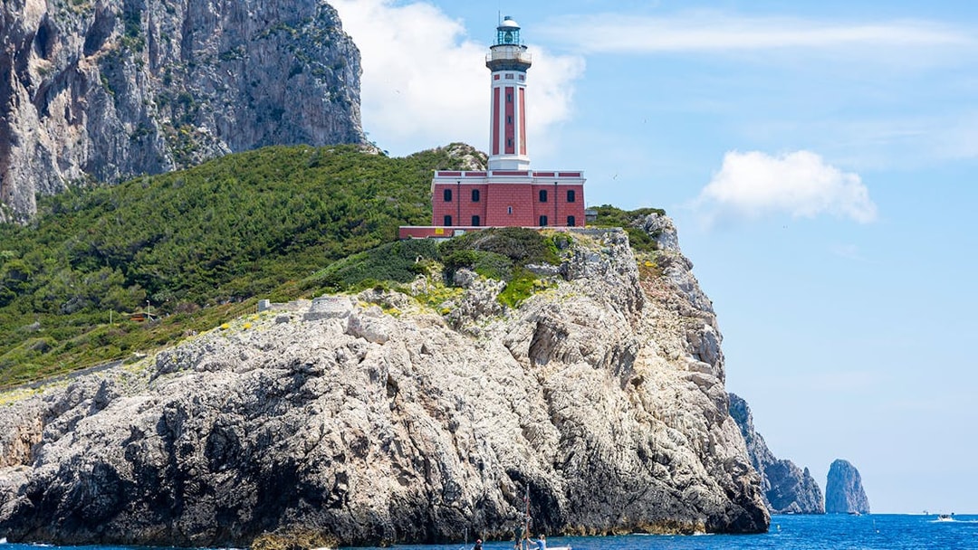 Lighthouse on rocky cliff with boat in Capri, Italy.