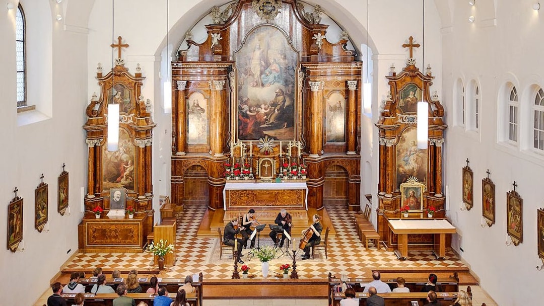 String quartet performing in Minoritenkirche, Vienna, with ornate altar backdrop.