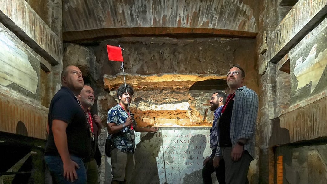 Visitors with guide inside Capuchin Crypt, Rome, observing ancient inscriptions.