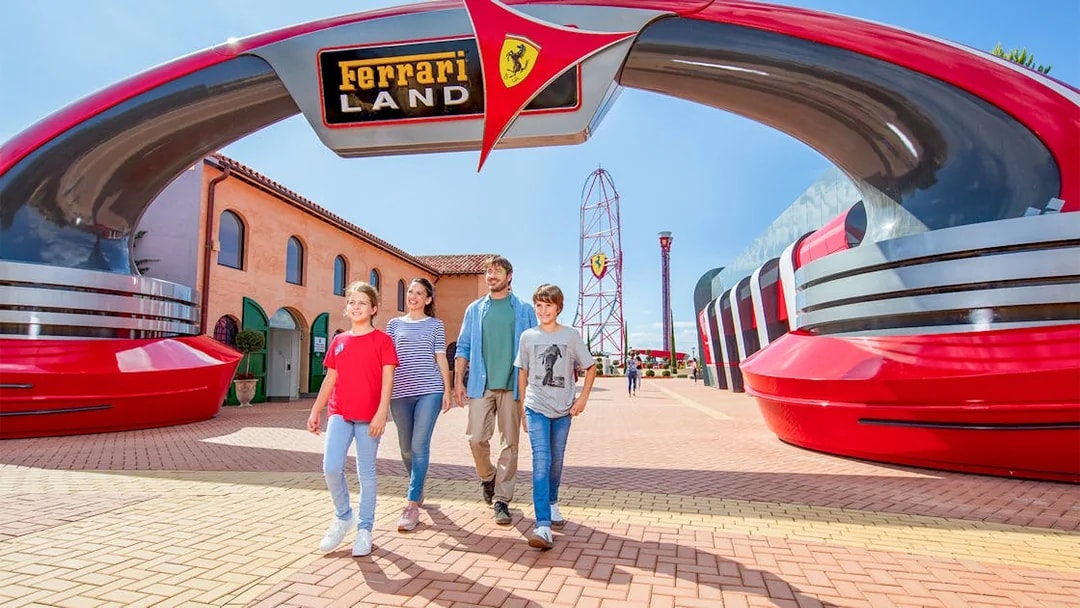 Family walking under Ferrari Land entrance at PortAventura World, with roller coaster in background.