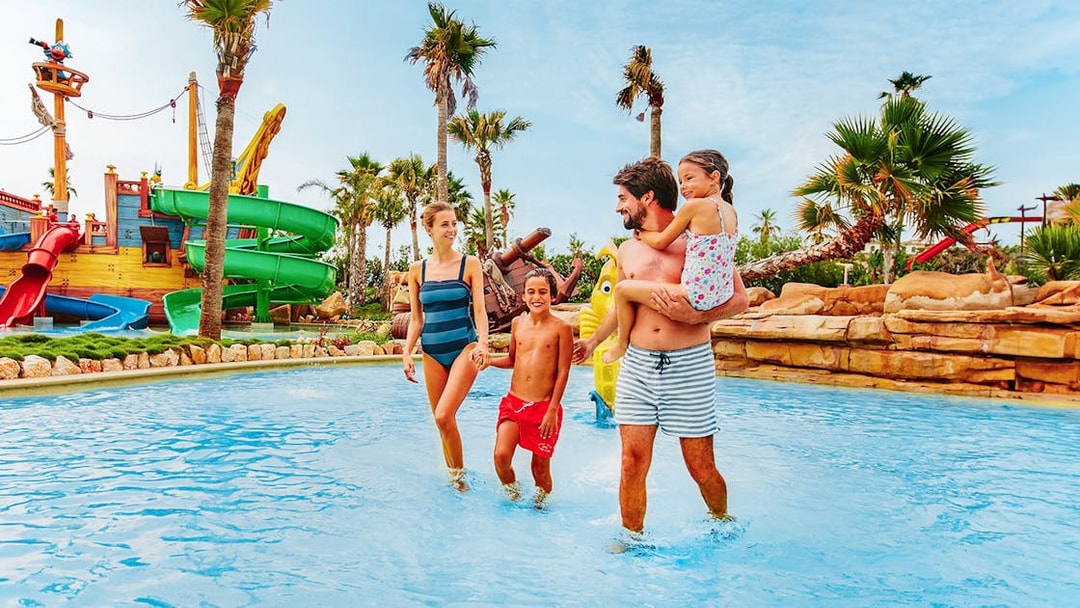 Family enjoying water play at Caribe Aquatic Park with slides and palm trees.
