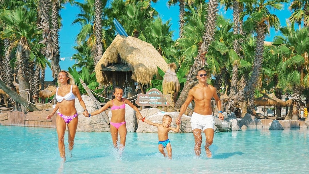 Family enjoying a day at Caribe Bay water park, running through a pool surrounded by palm trees.