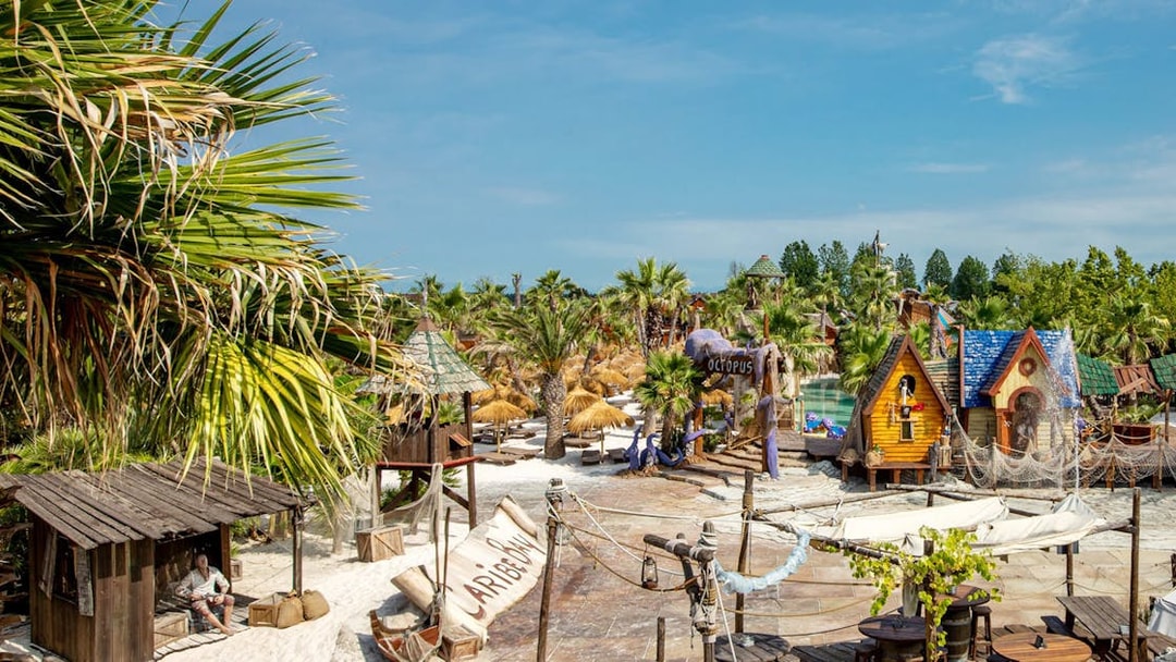 Caribe Bay entrance with tropical huts and palm trees in a water park setting.
