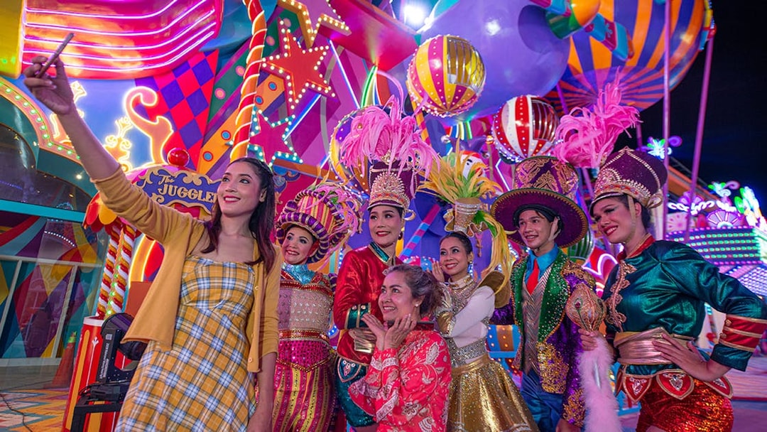 Carnival performers and visitors at Carnival Magic Park, vibrant costumes and lights.