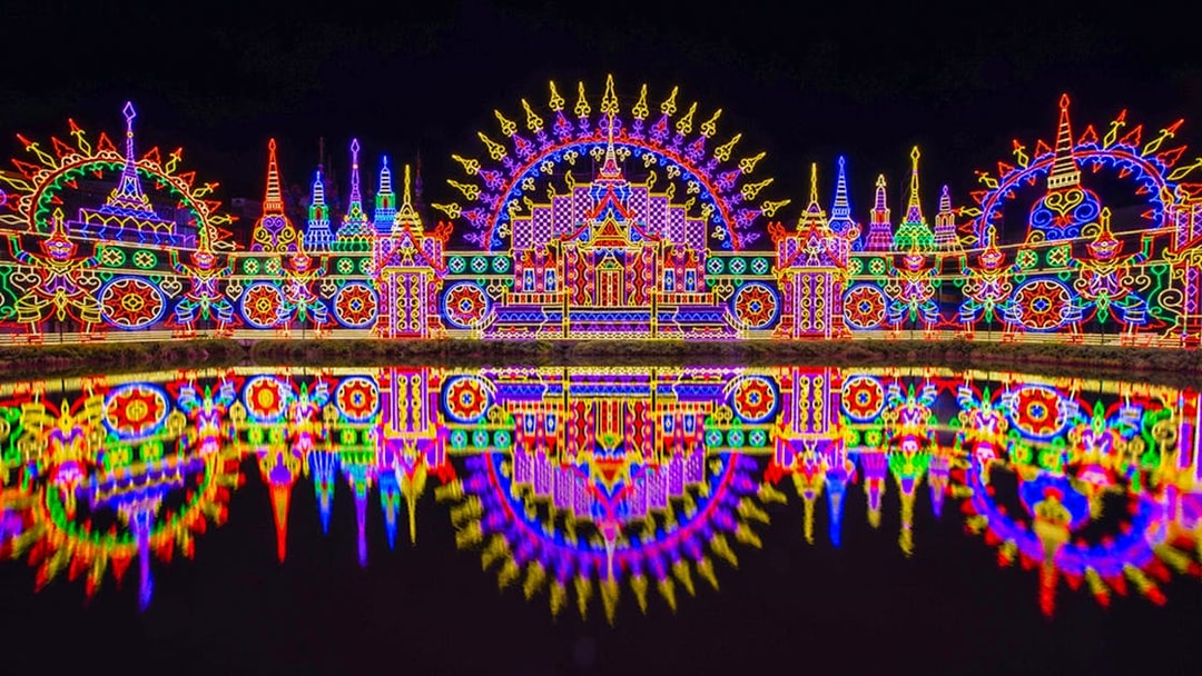 Colorful neon lights display at Carnival Magic Park, Phuket, reflecting in water.