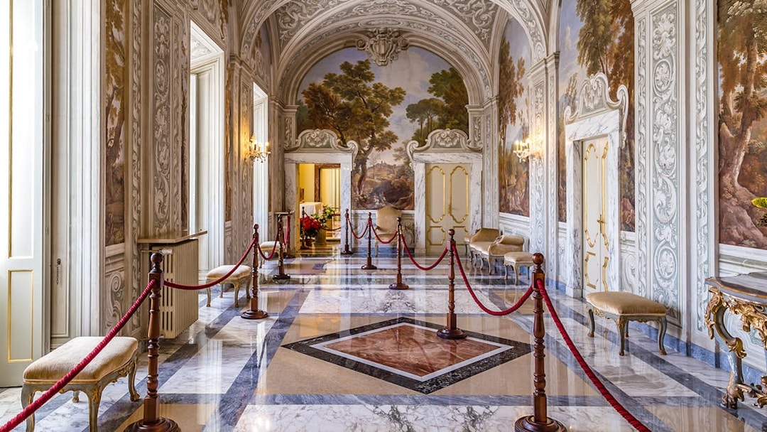 Ornate hallway inside Castle Gandolfo with frescoed walls and marble floors.