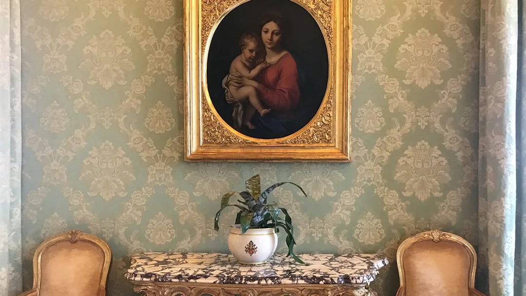 Painting and ornate table inside Castle Gandolfo with elegant chairs and wallpaper.