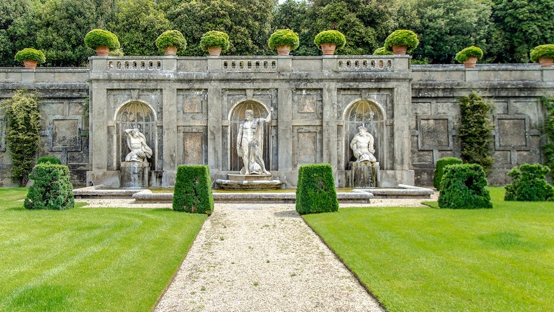 Sculptures in Pontifical Villa Gardens with manicured hedges and stone wall backdrop.