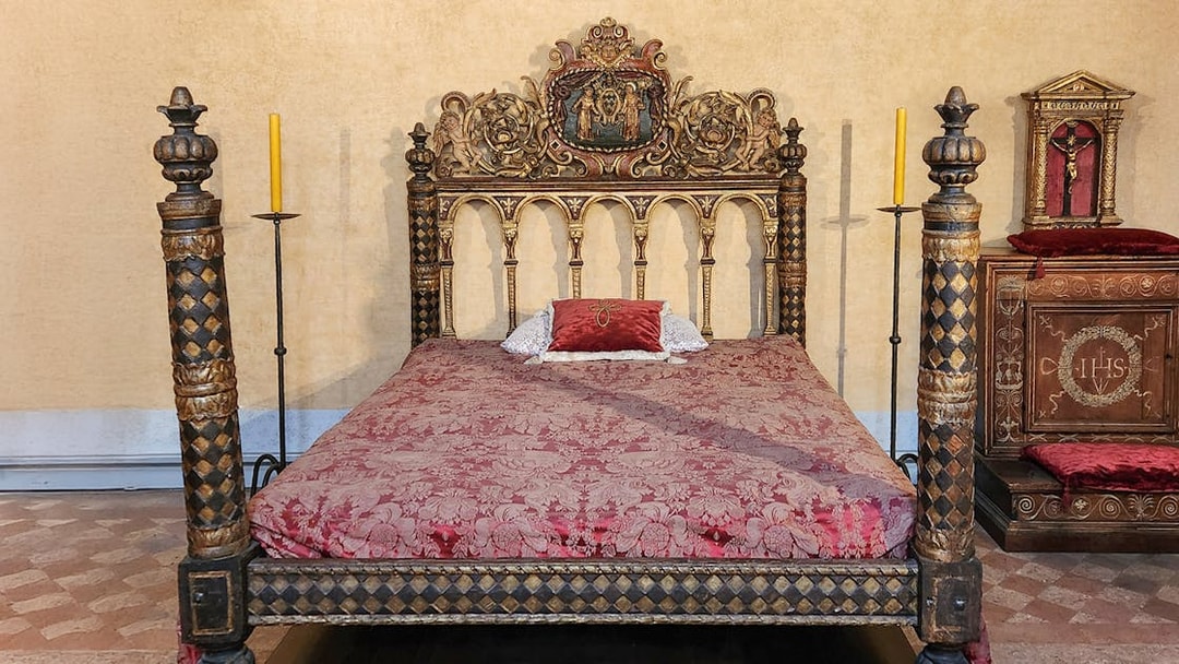 Ornate bed in Castel Sant'Angelo bedroom, Rome, with intricate carvings and red bedding.