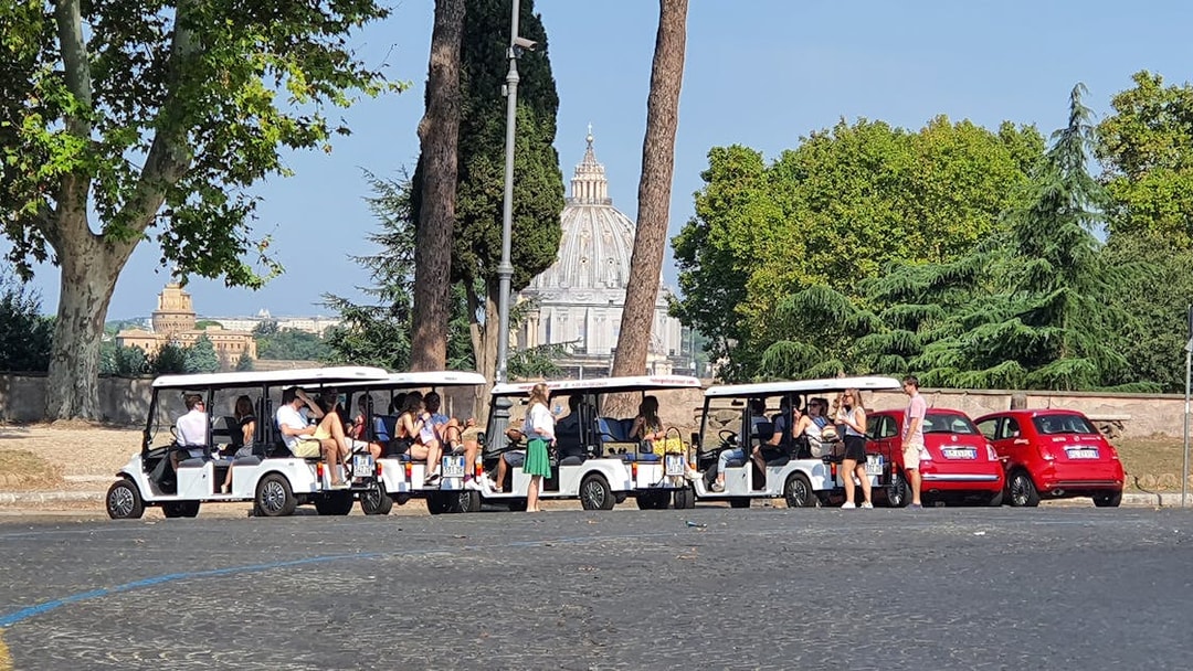 People touring Vatican City on golf carts with St. Peter's Basilica in the background.
