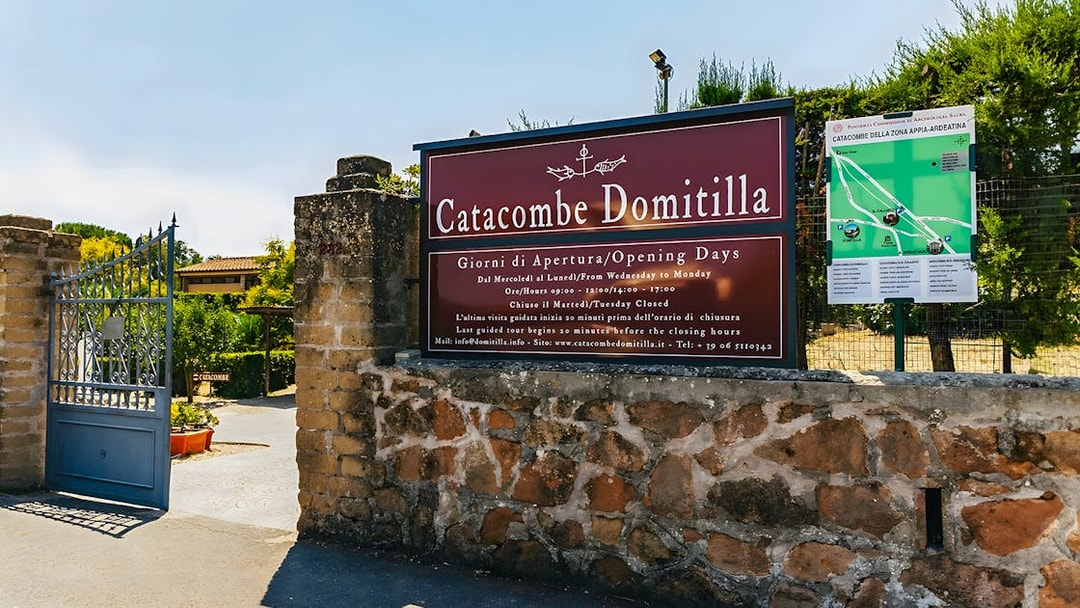 Entrance to Catacombs of Domitilla with sign displaying opening hours and map.