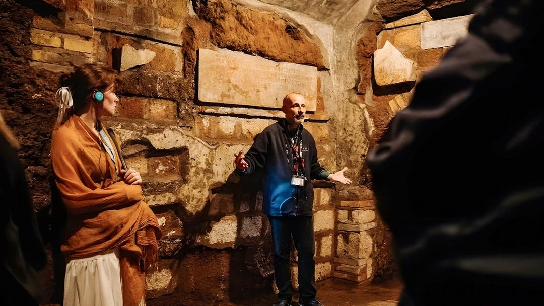 Guide explaining Roman Catacombs to tourists during Capuchin Crypts tour.
