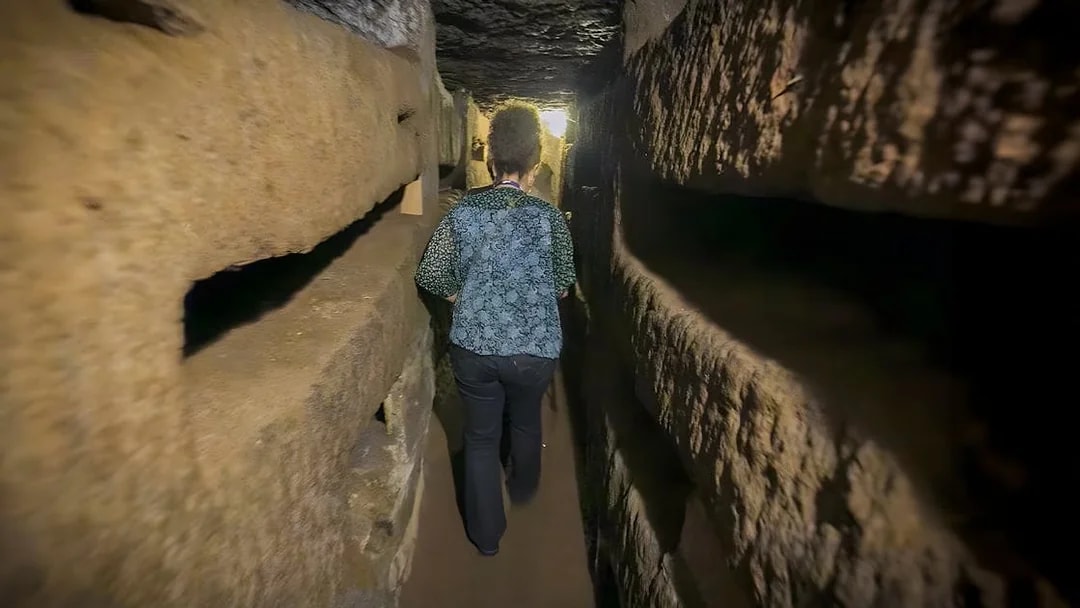 Person walking through narrow passage in Roman Catacombs during guided tour.