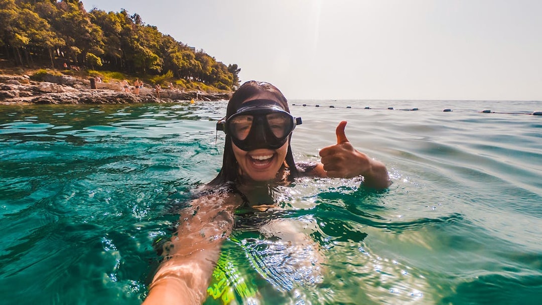 Snorkeler giving thumbs up in clear waters near Isole Ciclopi, Catania.