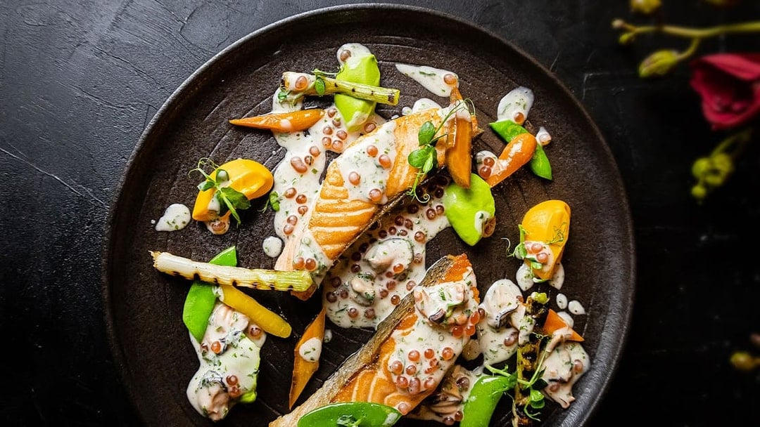 Salmon dish with vegetables and sauce at CÉ LA VI Dubai, featuring Burj Khalifa views.