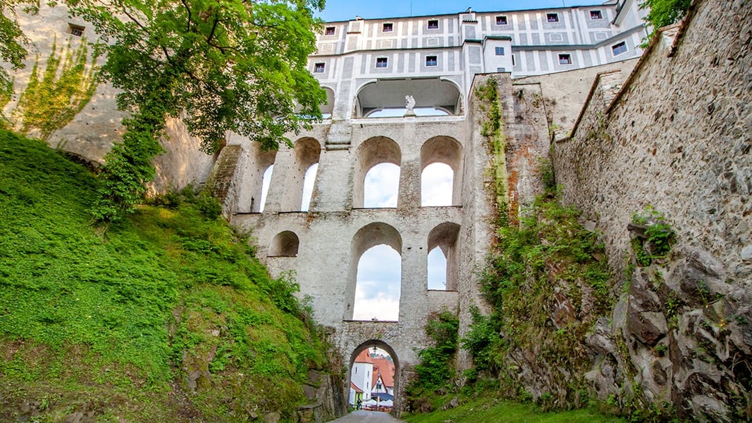 Bridge over Cesky Krumlov castle with stone arches and greenery.