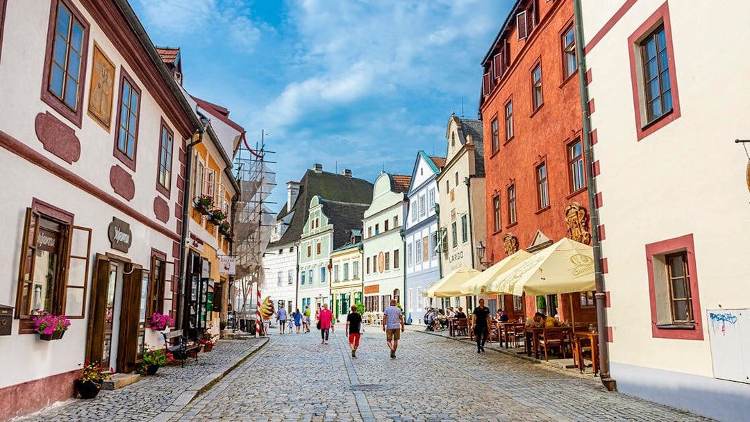 Tourists walking along a cobblestone street in Cesky Krumlov, surrounded by colorful historic buildings.