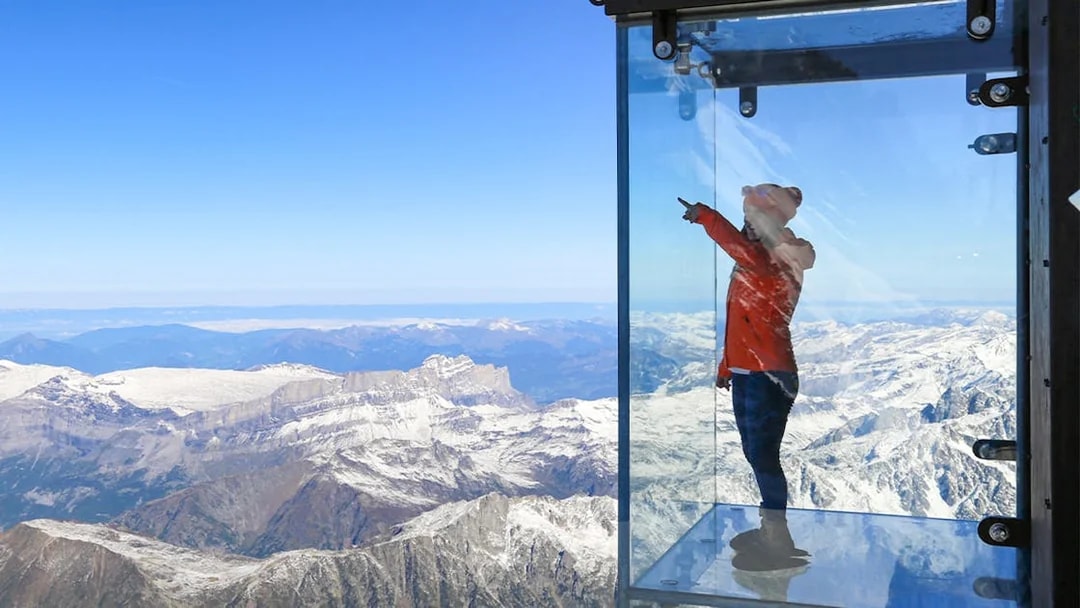 Person in glass box overlooking snowy Alps on Chamonix Mont Blanc day trip.