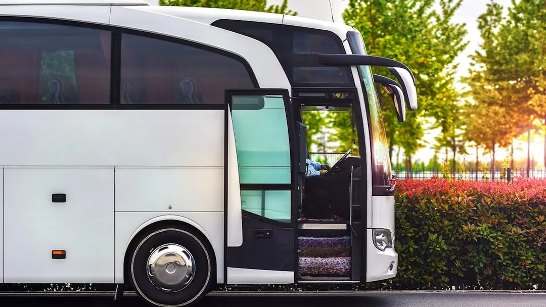 Amsterdam Airport Express bus parked with open door, surrounded by greenery.