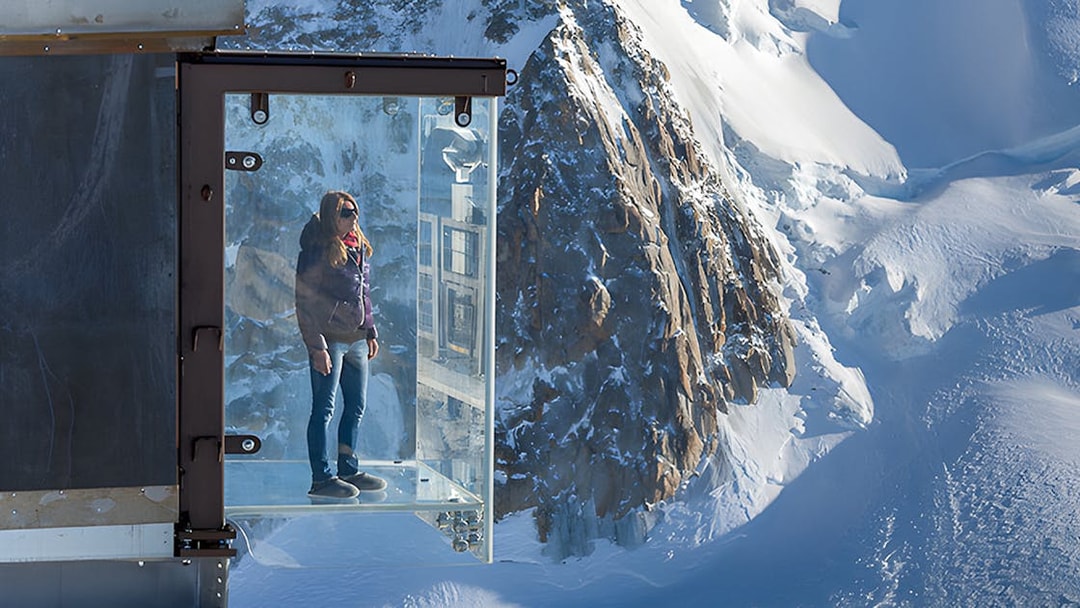 Person standing on a glass platform overlooking snowy peaks in Chamonix Mont Blanc.