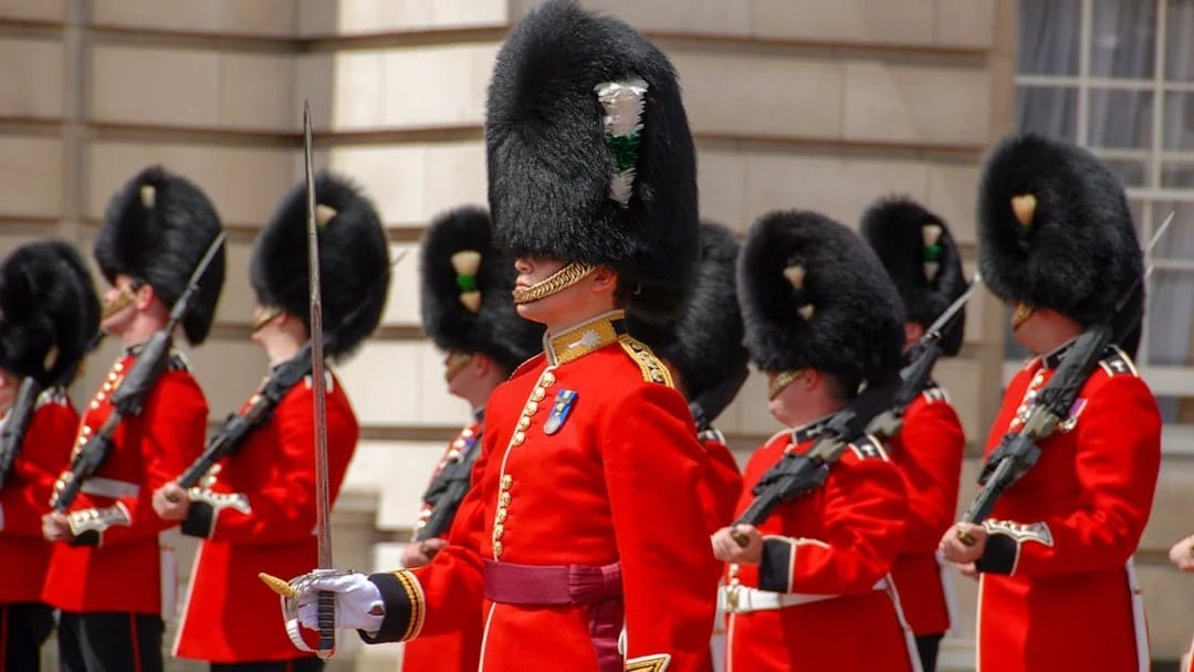 Guards in red uniforms and bearskin hats at Buckingham Palace ceremony.