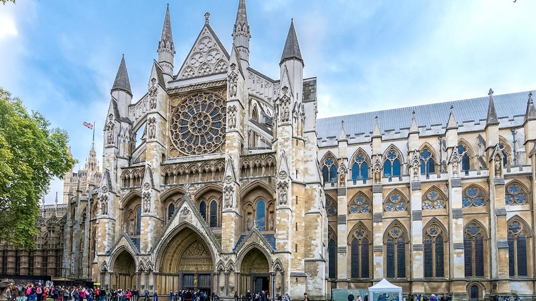 Westminster Abbey façade with rose window and tourists in London.