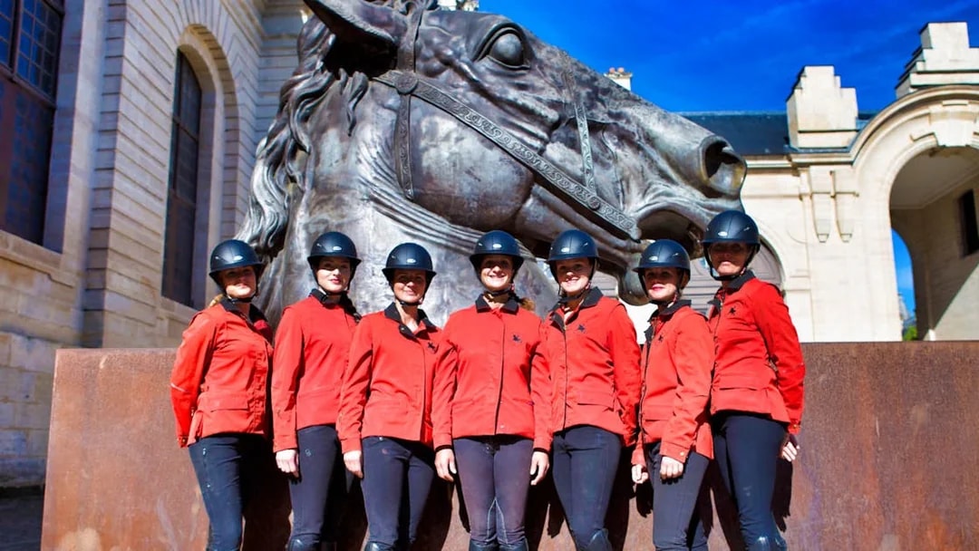 Equestrian team in red jackets at Chateau of Chantilly statue.