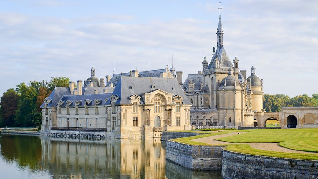 Chateau of Chantilly reflecting in water, showcasing its grand architecture.