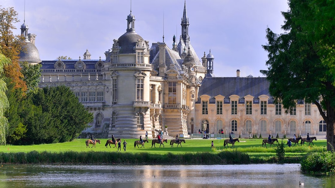 Chateau of Chantilly with visitors on horseback by the lake, France.