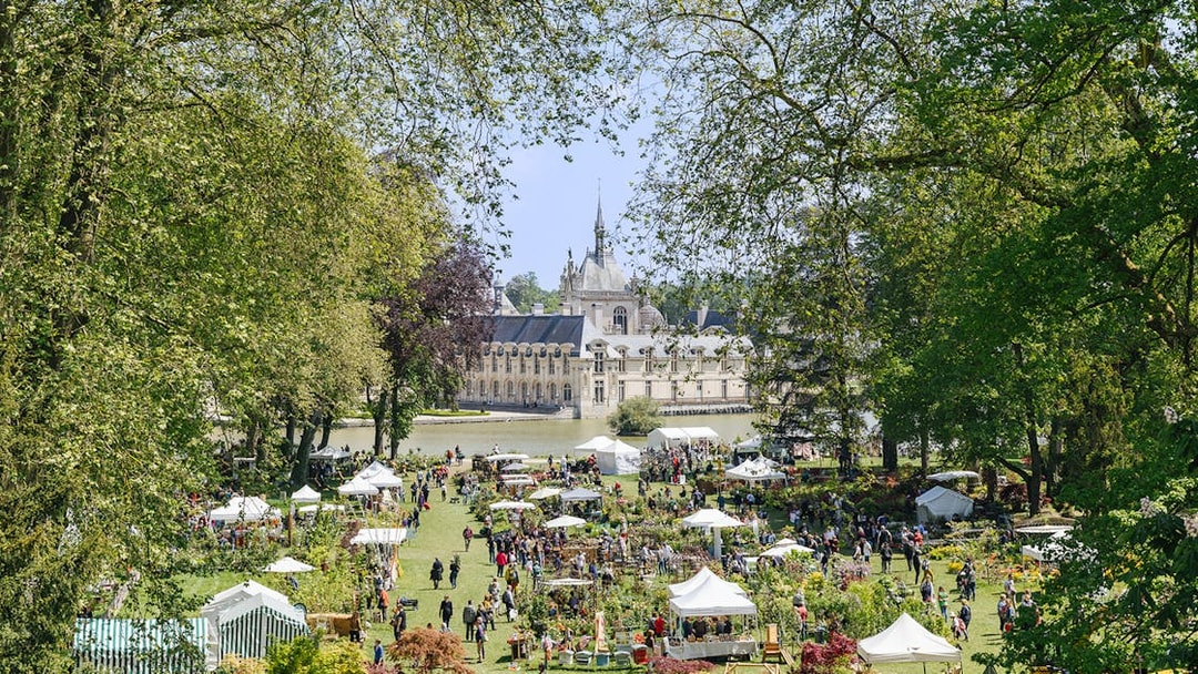 Chateau of Chantilly gardens with visitors and market stalls, France.
