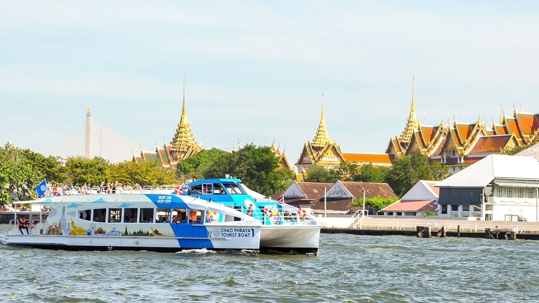 Tourists on Chao Phraya boat with Bangkok temples in the background.