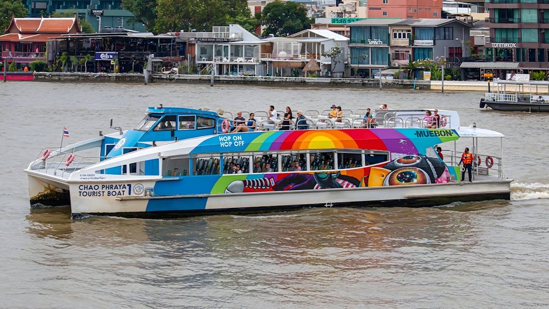 Chao Phraya tourist boat on Bangkok river with colorful design and passengers on deck.