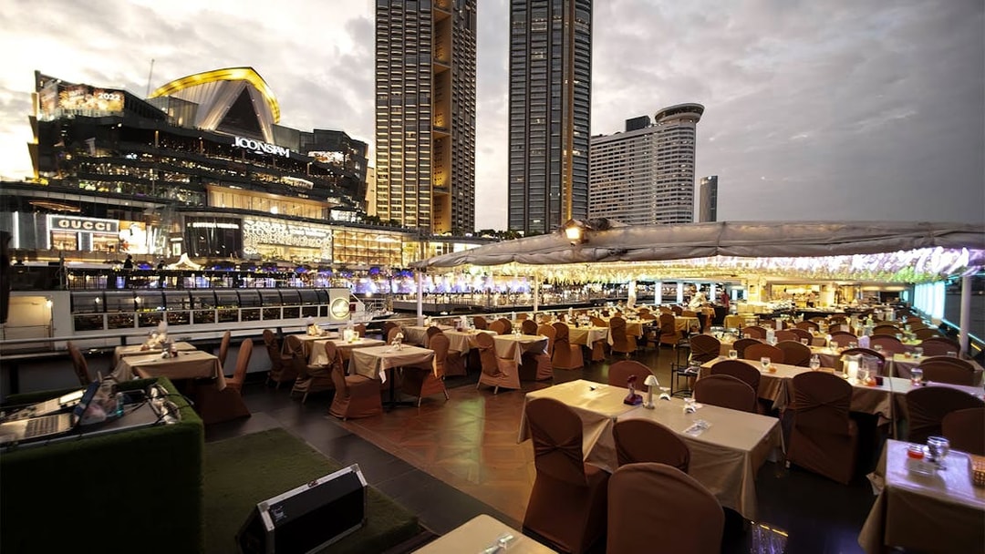 Dinner tables set on Chao Phraya Princess Cruise with Bangkok skyline in view.