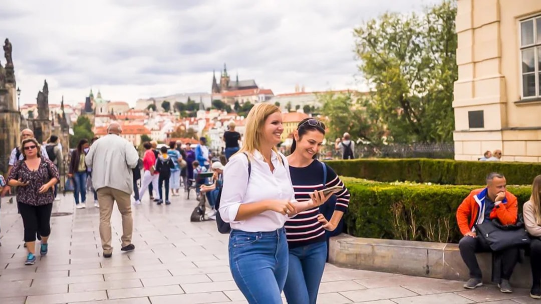 Tourists exploring Charles Bridge with Prague Castle in the background.