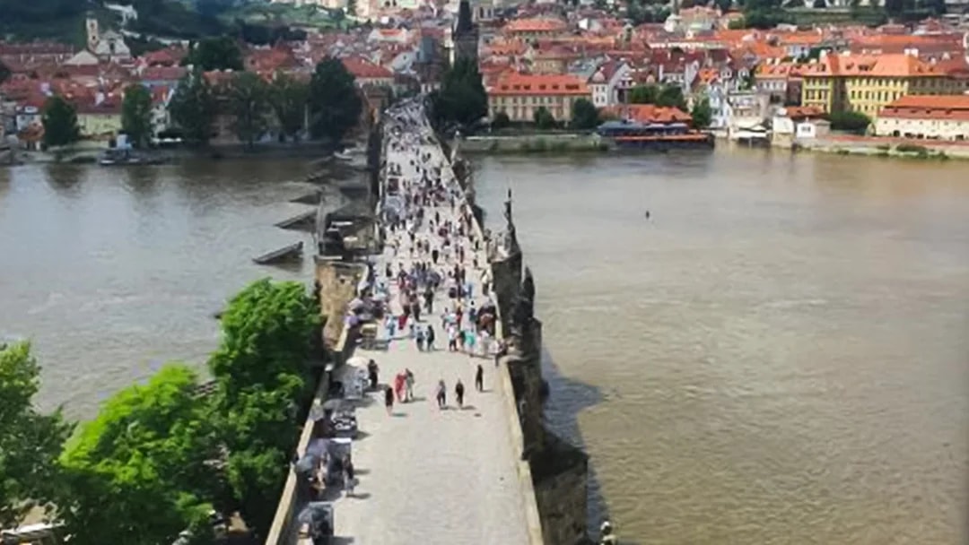 Crowds walking on Charles Bridge in Prague with cityscape views.