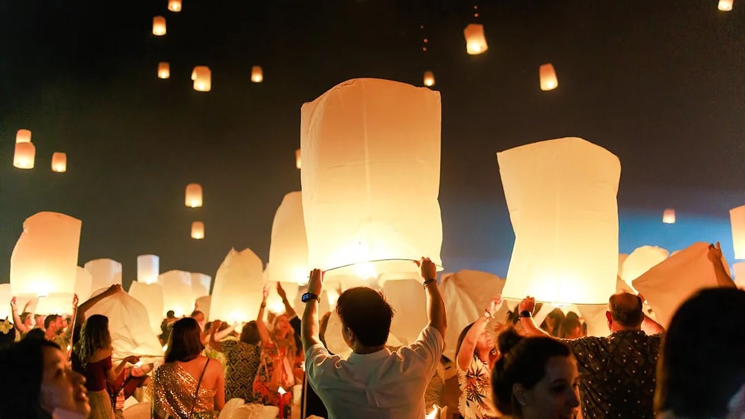 People releasing lanterns into the night sky at Chiang Mai Sky Lanterns Festival 2025.