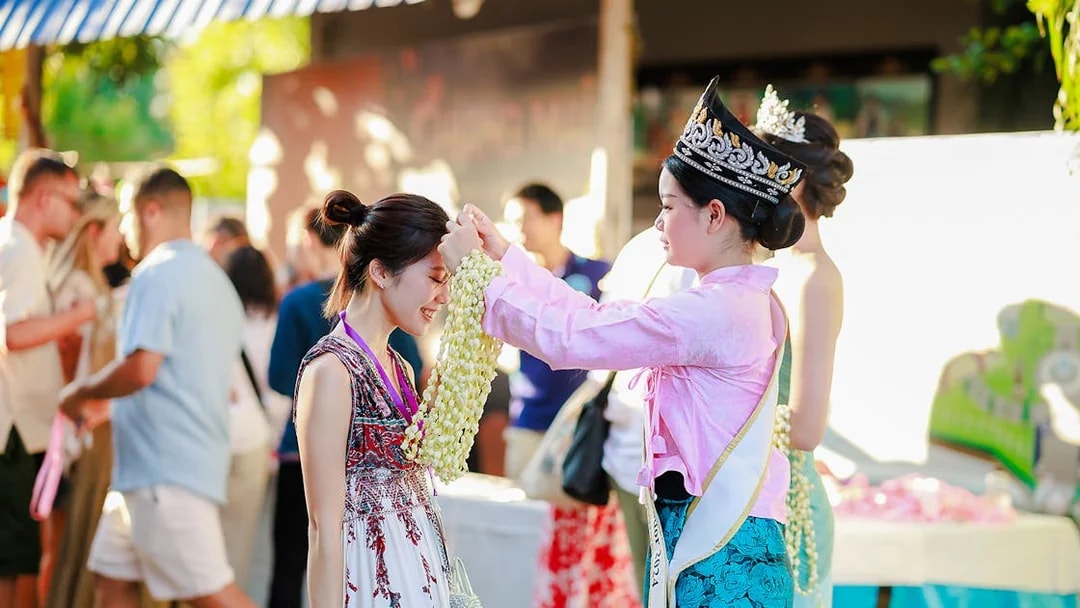 Ambassador in Thai attire presents jasmine garland to visitor at Sky Lanterns Festival.