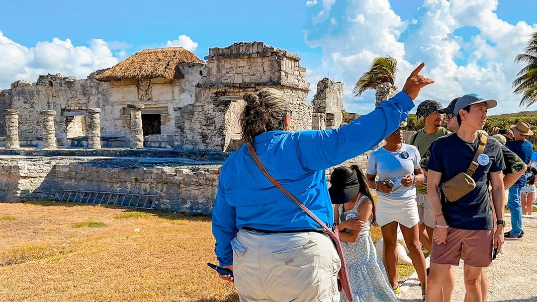 Tour guide explaining Tulum stone temple and ruins to tourists.