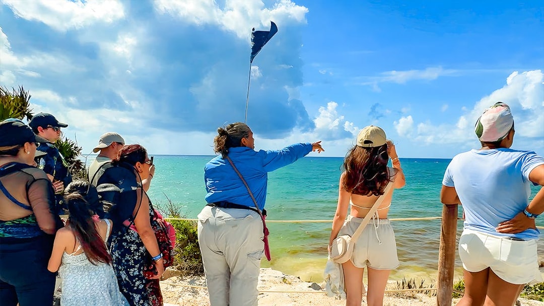 Tourist guide pointing at Tulum Beach with group of tourists.