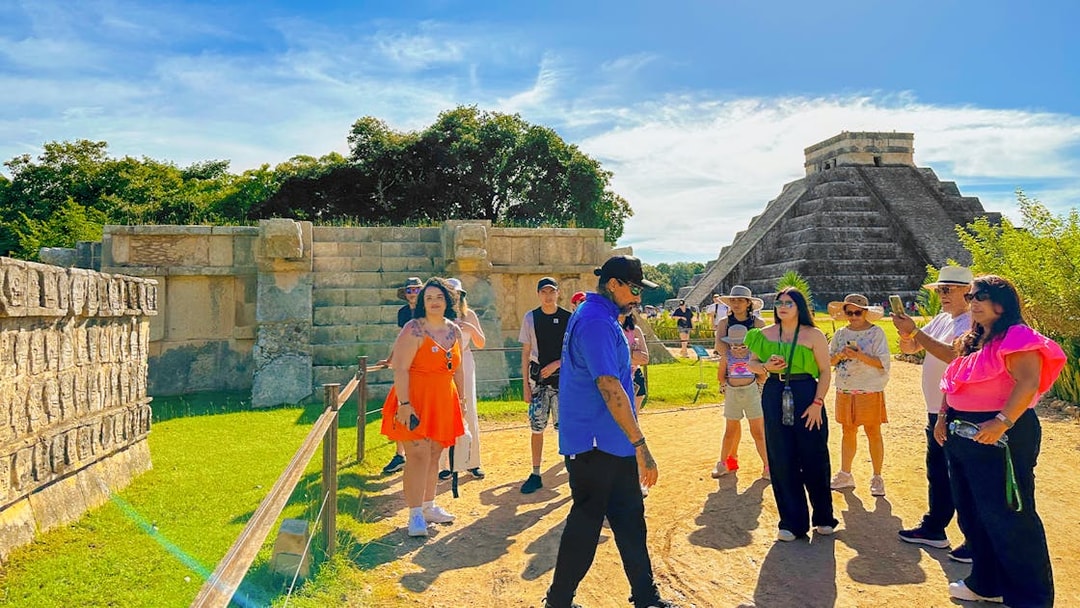 Tour guide explaining Chichen Itza temple and nearby ruins to a group of visitors.