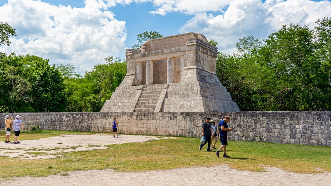 Tourists exploring ancient structure at Chichen Itza during sunrise.