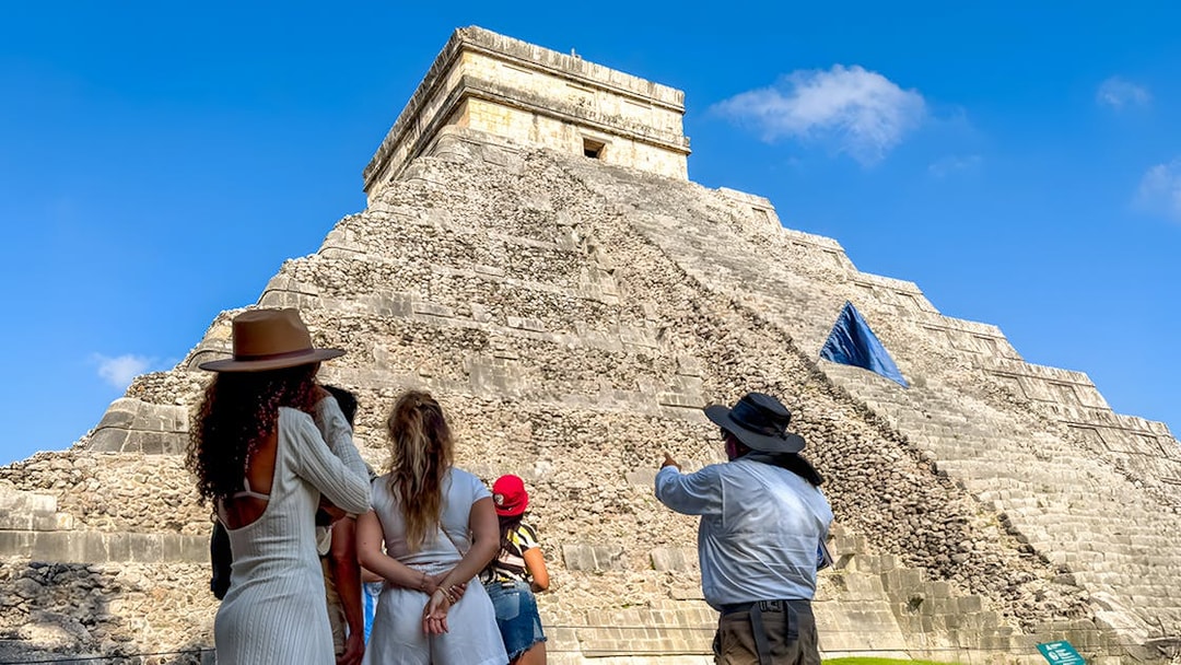 Tourist guide explaining Chichen Itza temple to visitors under a clear blue sky.
