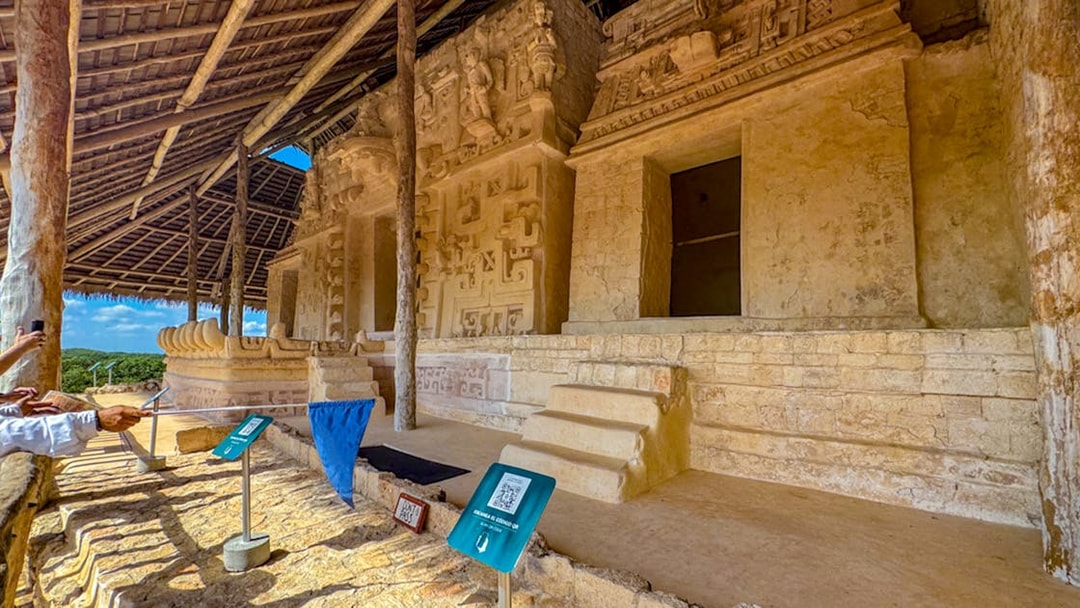 Ek Balam archaeological site with ancient stone carvings and steps under a thatched roof.