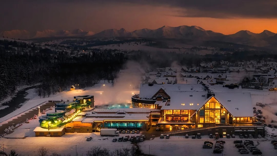 Chocholow Thermal Baths Saunarium at dusk with snow-covered landscape.