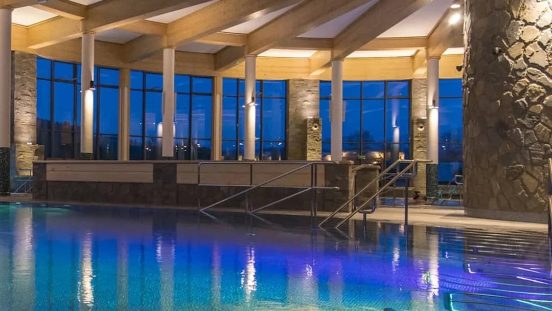 Chocholow Thermal Baths Saunarium pool with stone pillars and large windows at dusk.