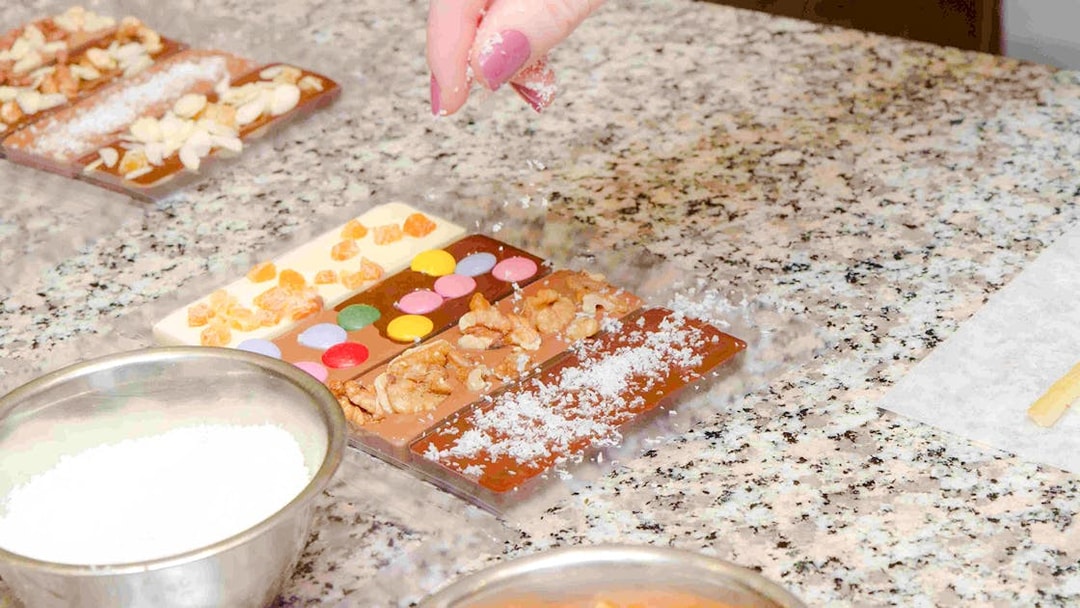 Hand decorating chocolate bars with nuts and candies at Choco-Story Paris.
